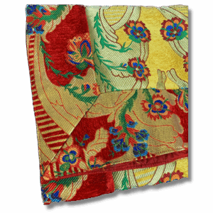 Colourful Tibetan brocade altar cloth with red trim and floral patterns in gold, red, blue, and green, folded for shrine or table decoration.