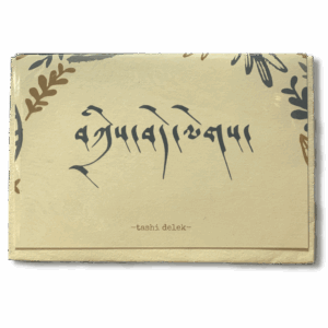 Hand-printed greeting card featuring Tibetan calligraphy reading “Tashi Delek” (good wishes) with subtle leaf motifs on a cream background.