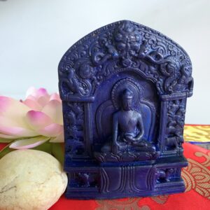 Blue resin statue of the Enlightenment Buddha, handmade in Nepal, displayed against a decorative background with a pink flower and a red and yellow textile.