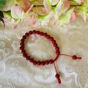 A faux red coral wrist mala with 25 beads and two hanger beads, displayed on a lace-patterned surface.