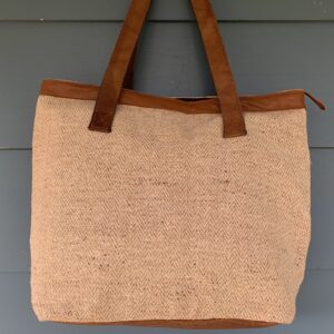 A handmade hemp tote bag with brown imitation leather straps and a brown cotton lining, displayed against a blue background.