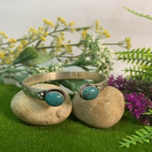 Two stacked bracelets with turquoise-like stones and silver detailing, handmade, displayed on a rock surrounded by greenery.