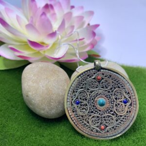 A large brass amulet pendant with filigree metal and a brass endless knot design, displayed against a floral background.