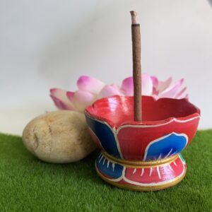 Hand painted wooden incense holder in the shape of a lotus flower, displayed on a grass-like surface with a artificial lotus flower and a rock in the background.