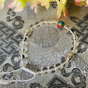 A clear crystal wrist mala with decorative beads and metal spacers laid out on a patterned surface.