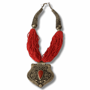 Red beaded necklace with ornate silver-tone pendant featuring a teardrop red stone, Tibetan-style metalwork details, and decorative curved metal end pieces.