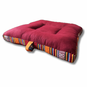 A square meditation cushion in maroon color with a geometric pattern along the edges and a carrying loop.