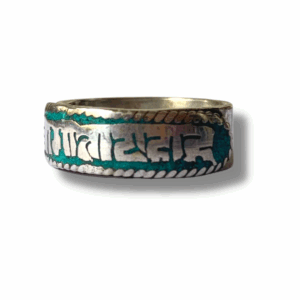 Close-up of a round silver-tone ring engraved with Sanskrit script around the band, resting on a soft light-grey surface.