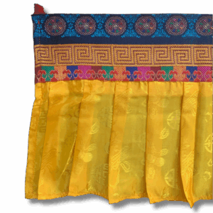 Close-up of yellow Tibetan shambu ruffled banner with multicoloured brocade trim and embroidered auspicious symbols, used for shrine and altar decoration.